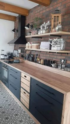 a kitchen with black cabinets and wooden shelves next to a brick wall that has open shelving above it