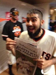 a man with a beard holding up a news paper while another man looks at the camera