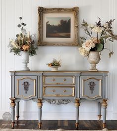 two vases with flowers sit on top of an antique dresser in front of a painting