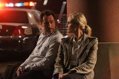 a man and woman sitting next to each other on a bench in front of parked cars