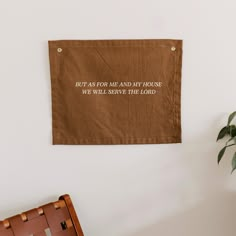 a brown wall hanging on the side of a white wall next to a chair and potted plant