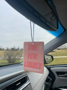 a pink sign that says live for christ hangs from the dash board of a car