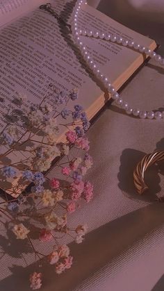 an open book with pearls and flowers on it next to a necklace, bracelet and ring