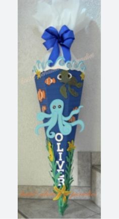 an octopus themed vase with tissue paper and blue ribbon tied around the top, sitting on a tile floor