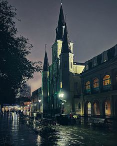 an old church lit up at night with people walking around the street in the rain