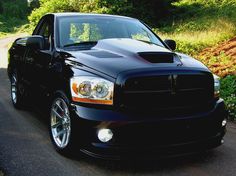 a black truck parked on the side of a road next to grass and bushes with trees in the background