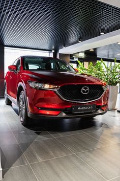 a red mazda cx - 5 parked in a showroom with potted plants