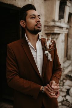 a man wearing a brown suit and white shirt standing in front of an old building