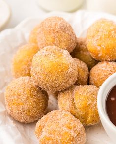 some sugared doughnuts and dipping sauce on a white paper towel next to it