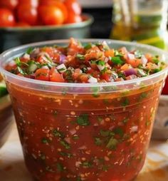 a plastic container filled with salsa sitting on top of a table next to other vegetables