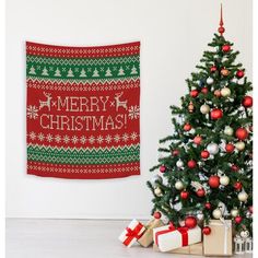 a christmas tree with presents under it next to a red and green tapestry hanging on the wall