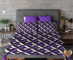 a bed with purple and black comforters in a room next to a brick wall