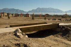 a wooden bench sitting in the middle of a dirt field with mountains in the background