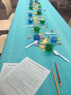 the long table is set up with plastic cups and paper utensils on it