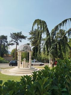 a gazebo in the middle of a park surrounded by greenery and parked cars