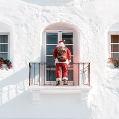 a man dressed as santa claus on the balcony of a white house with red shutters