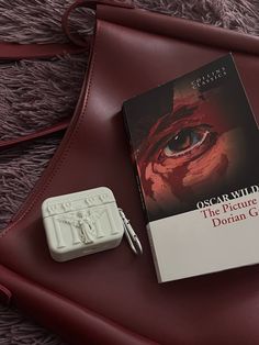 an open book sitting on top of a red bag next to a white plastic object