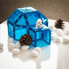 there is a small blue ice house and pine cones on the table