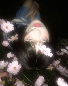 a woman with long black hair laying on top of white and pink daisies in the grass