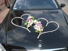 a black car with two hearts and flowers on it's front hood, parked in the street