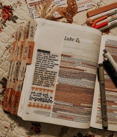 an open bible on a quilt with markers and pens next to it, along with other items