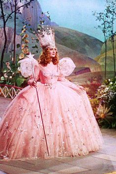 an old photo of a woman in a pink dress and tiara holding a cane