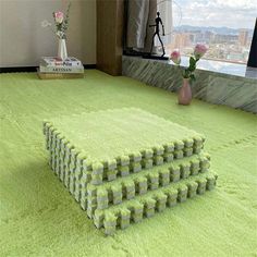 a pile of green carpet sitting on top of a floor next to a vase filled with flowers