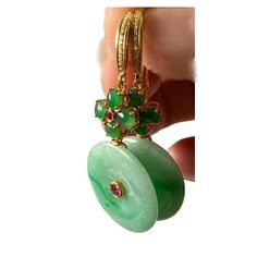 These stunning 18k gold art deco earrings showcase a large 100% round jadeite jade stone accented by centered ruby stone . Four additional round jade stones create a floral design, with a centered ruby and pave diamond on top. Measuring 2" in height and 1" in width, with a depth of 0.50", these earrings exude sophistication and elegance. Fine Jewelry Jade With 17 Jewels, Round Jade Jewelry With Matching Earrings, Luxury Green Jade Earrings, Exquisite Green Jade Jewelry, Yellow Gold Jade Earrings, Round Jade Earrings For Anniversary, Fine Jewelry: Hallmarked Jade, Fine Jewelry Earrings With Natural Stones, Traditional Yellow Gold Jade Jewelry