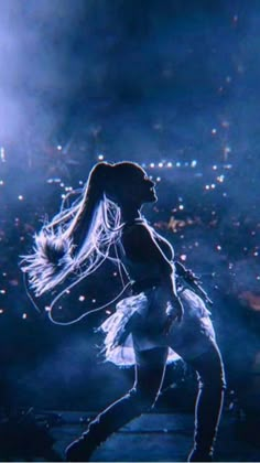 a woman is dancing on stage with headphones in her ears and lights behind her