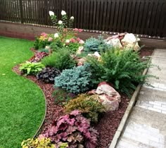 a garden filled with lots of different types of flowers and plants next to a wooden fence