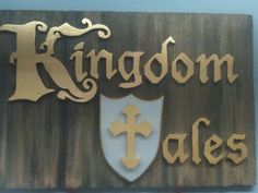 a wooden sign that says kingdom tales with a cross and shield on the bottom right hand corner