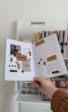 a person holding an open planner in front of a bookshelf with various items on it