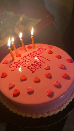 a pink birthday cake with hearts on it and candles in the shape of heart shapes