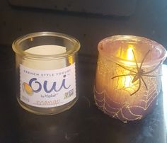 a candle is next to a glass jar with a spider on it and the label says ouu