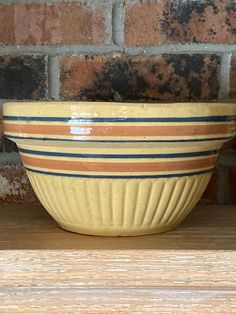 a yellow bowl sitting on top of a wooden table next to a brick wall and shelf