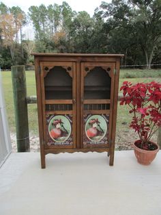 a wooden cabinet sitting on top of a cement floor next to a potted plant