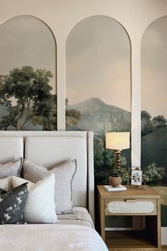 a large bed sitting under three arched windows next to a wall with paintings on it