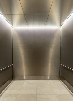 an empty room with metallic walls and tile flooring in the center is illuminated by recessed lighting