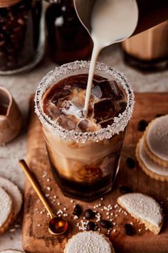 an iced drink being poured into a glass on top of a cutting board with cookies