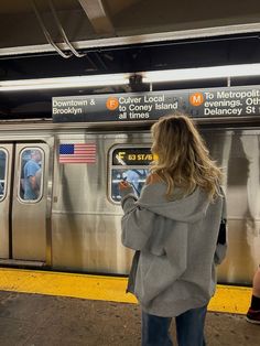 a woman looking at her cell phone while standing in front of a subway train platform