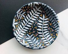 a black and white bowl with leaves painted on the side is sitting on a table