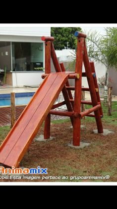 a wooden swing set with a slide in the back yard next to a swimming pool