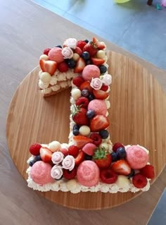 a cake shaped like the number one made out of fruit on a wooden platter