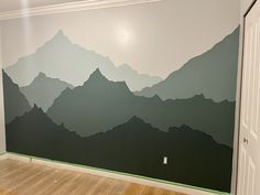 an empty room with mountains painted on the wall and wood flooring in front of it