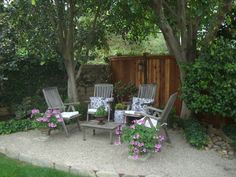 some chairs are sitting in the middle of a small yard with trees and flowers around them