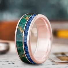 two wedding bands with blue and green marble inlays on each band, one is pink gold