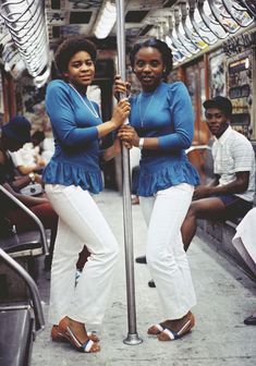 two women standing next to each other on a subway train holding onto a pole with their hands