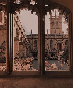 an open window looking out onto a building with flowers in the foreground and a clock tower in the background