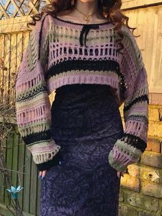 a woman standing in front of a wooden fence wearing a purple sweater and black skirt