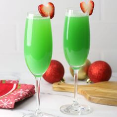 two wine glasses filled with green liquid and strawberries on the rim, next to christmas decorations